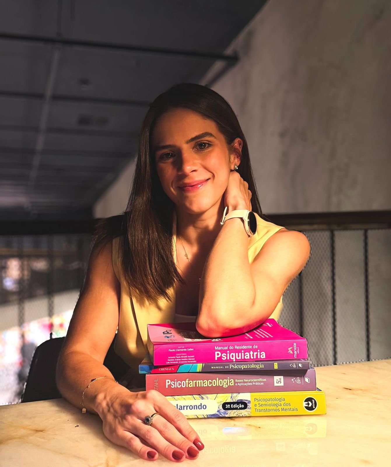Marina Braga sorrindo, apoiada em uma pilha de livros de psiquiatria